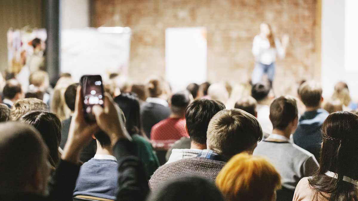People sitting in large room listening to speaker